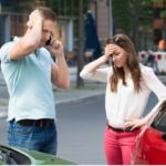 man talking on the phone standing next to a woman after a car accident